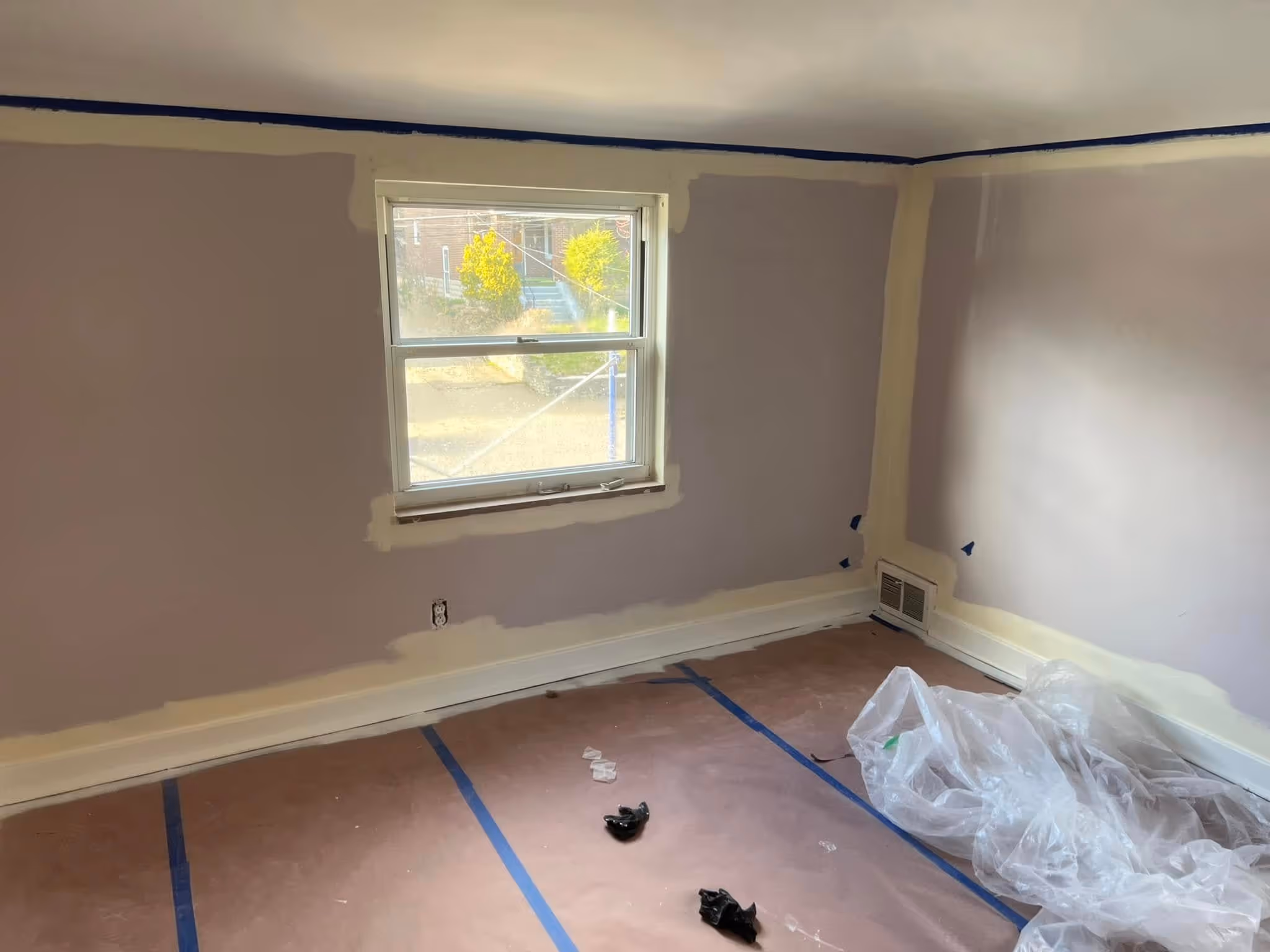 Room with freshly painted light purple walls and beige drywall joint patches around window and corners.