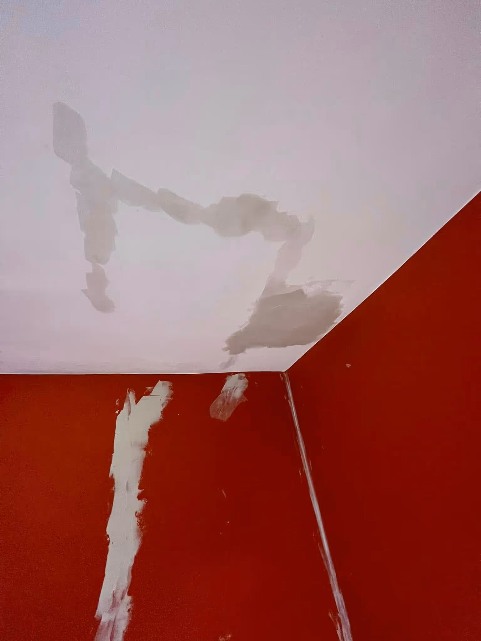 Corner of a room with red walls and a white ceiling showing multiple drywall patches in progress.