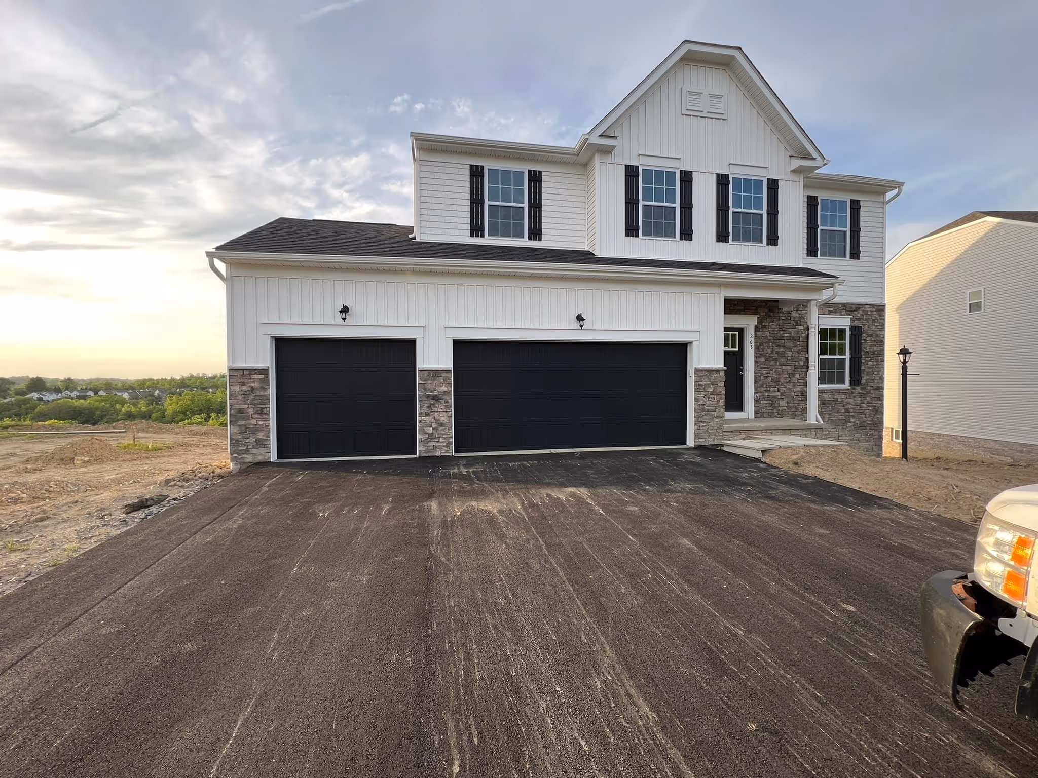 Newly built two-story house with white siding, black garage doors, stone accents, and a spacious driveway.