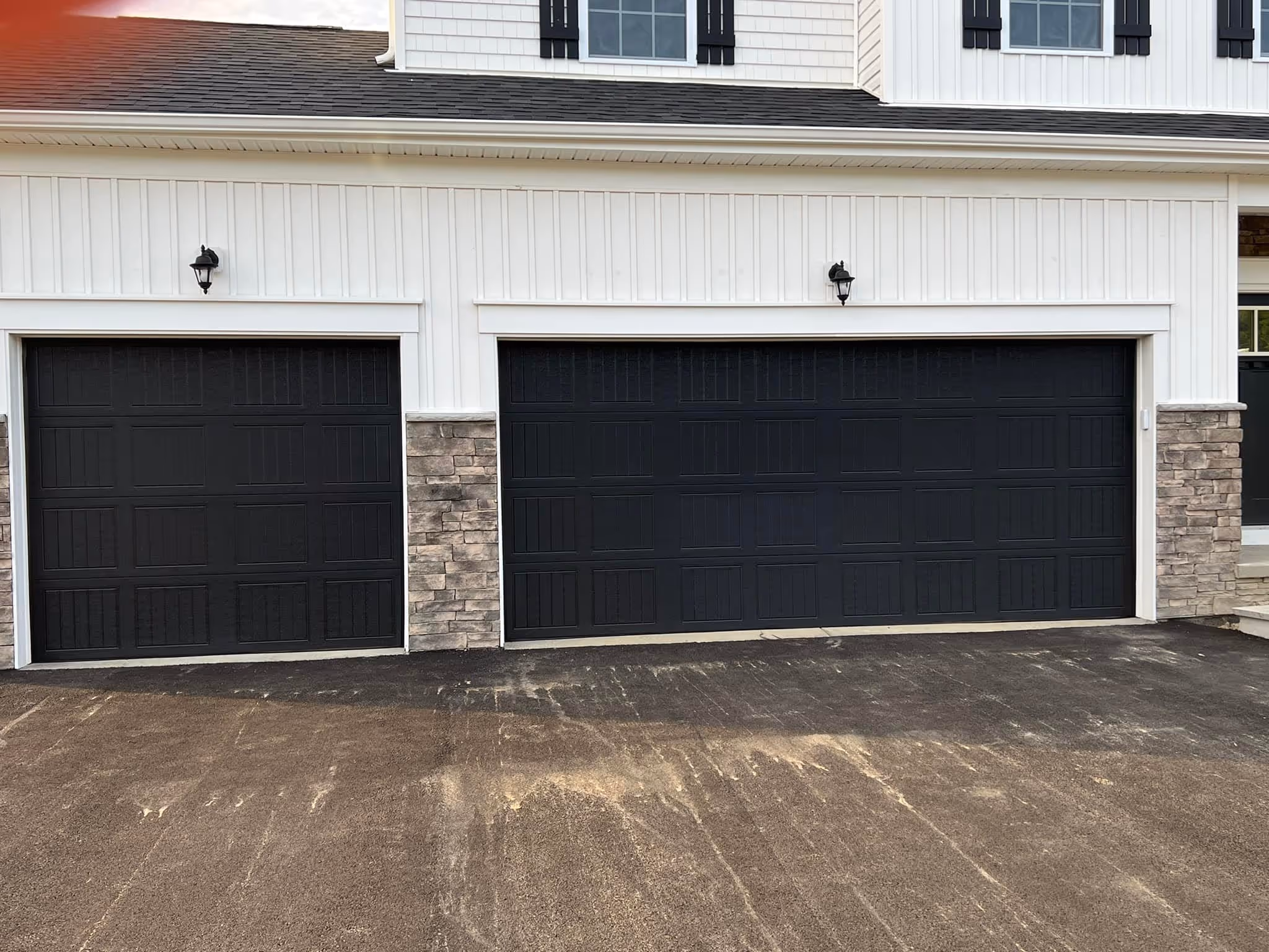 Modern house exterior with two black garage doors, stone accents, and white siding.