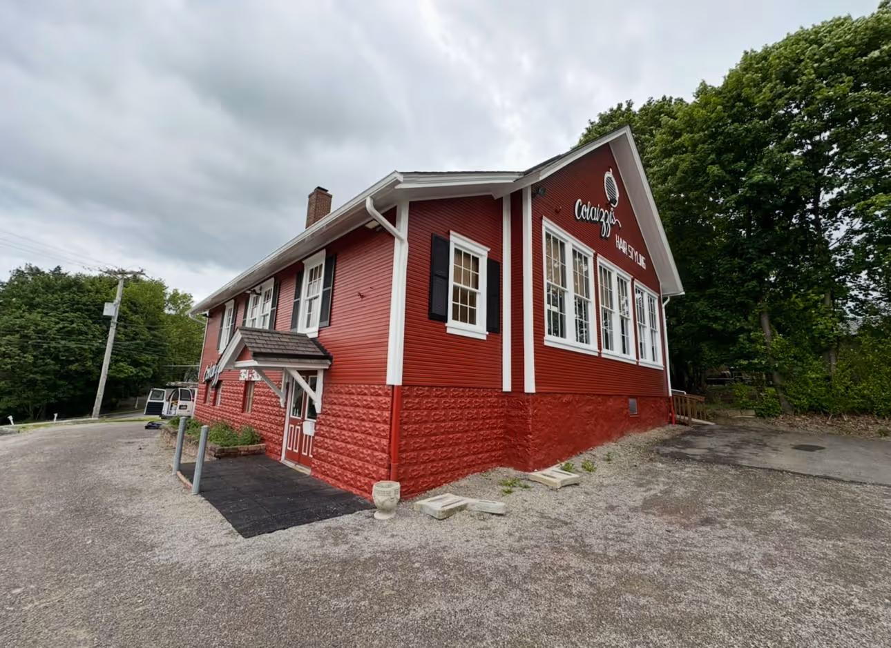 Red two-story building with white trim housing Colazzo Hair Style salon under a cloudy sky.