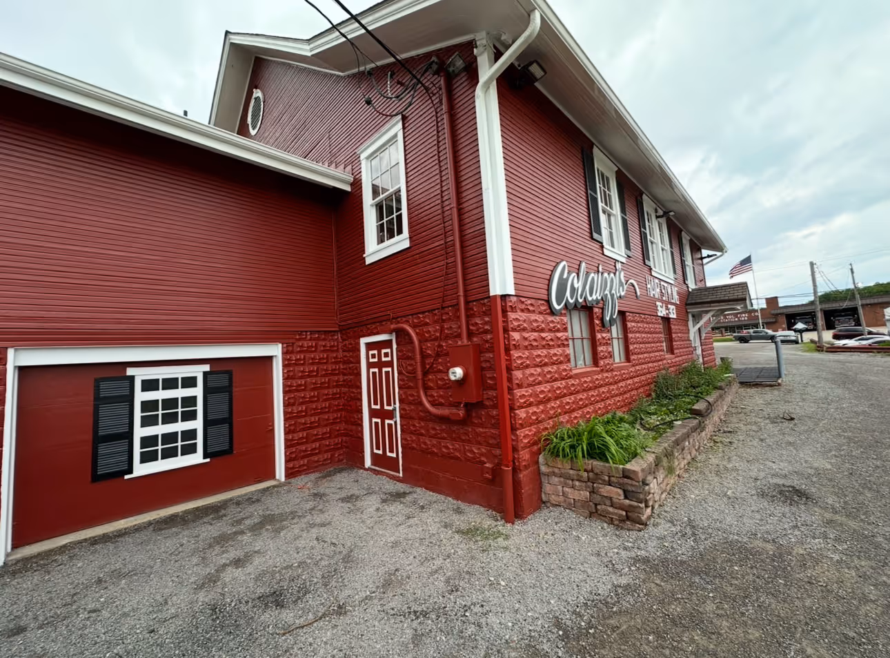 Red building with white-trimmed windows and doors, a sign reading Colaiuzo, and a gravel driveway.