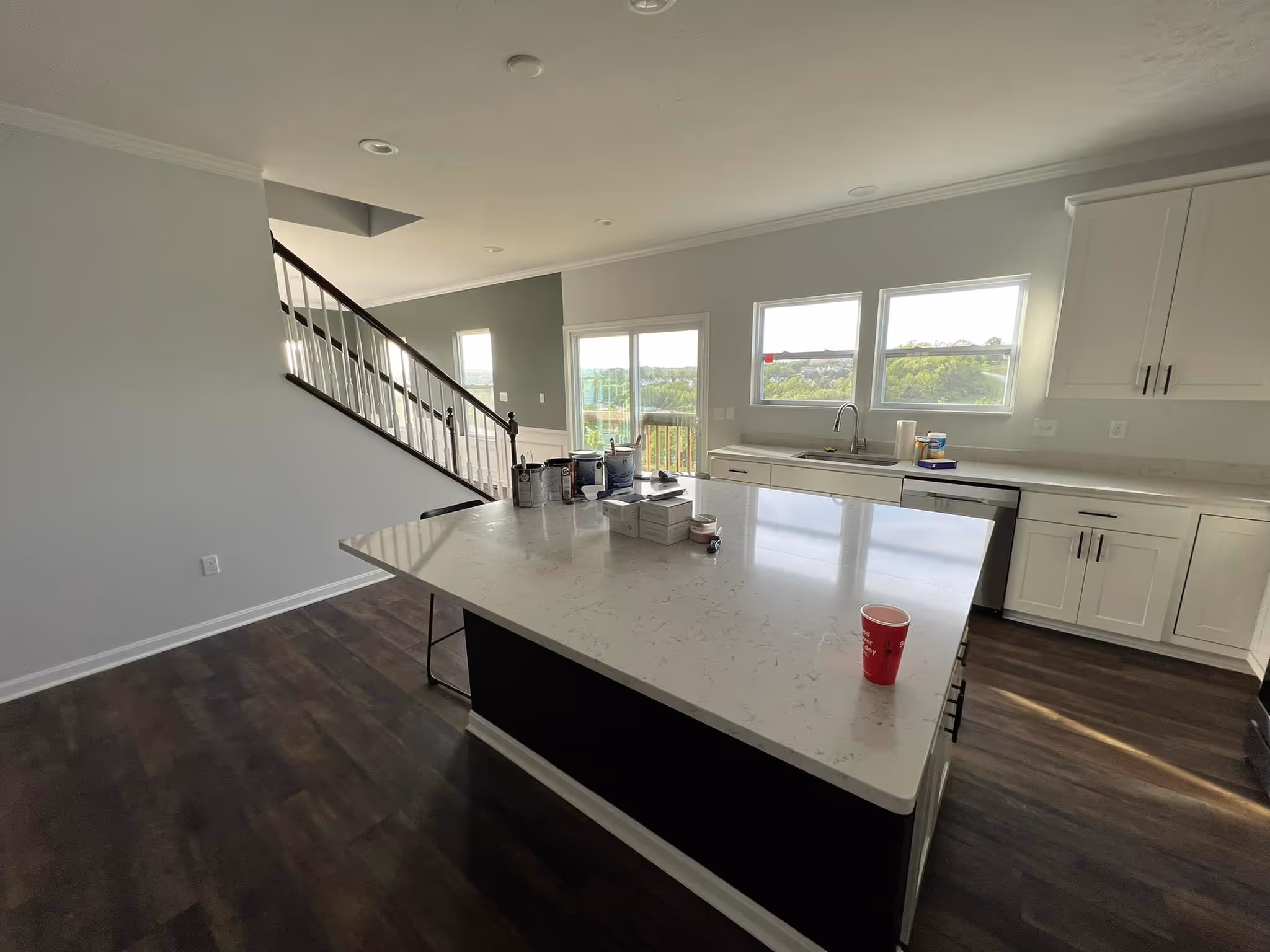 Modern kitchen with white cabinets, large island countertop, and dark wood flooring next to a staircase.