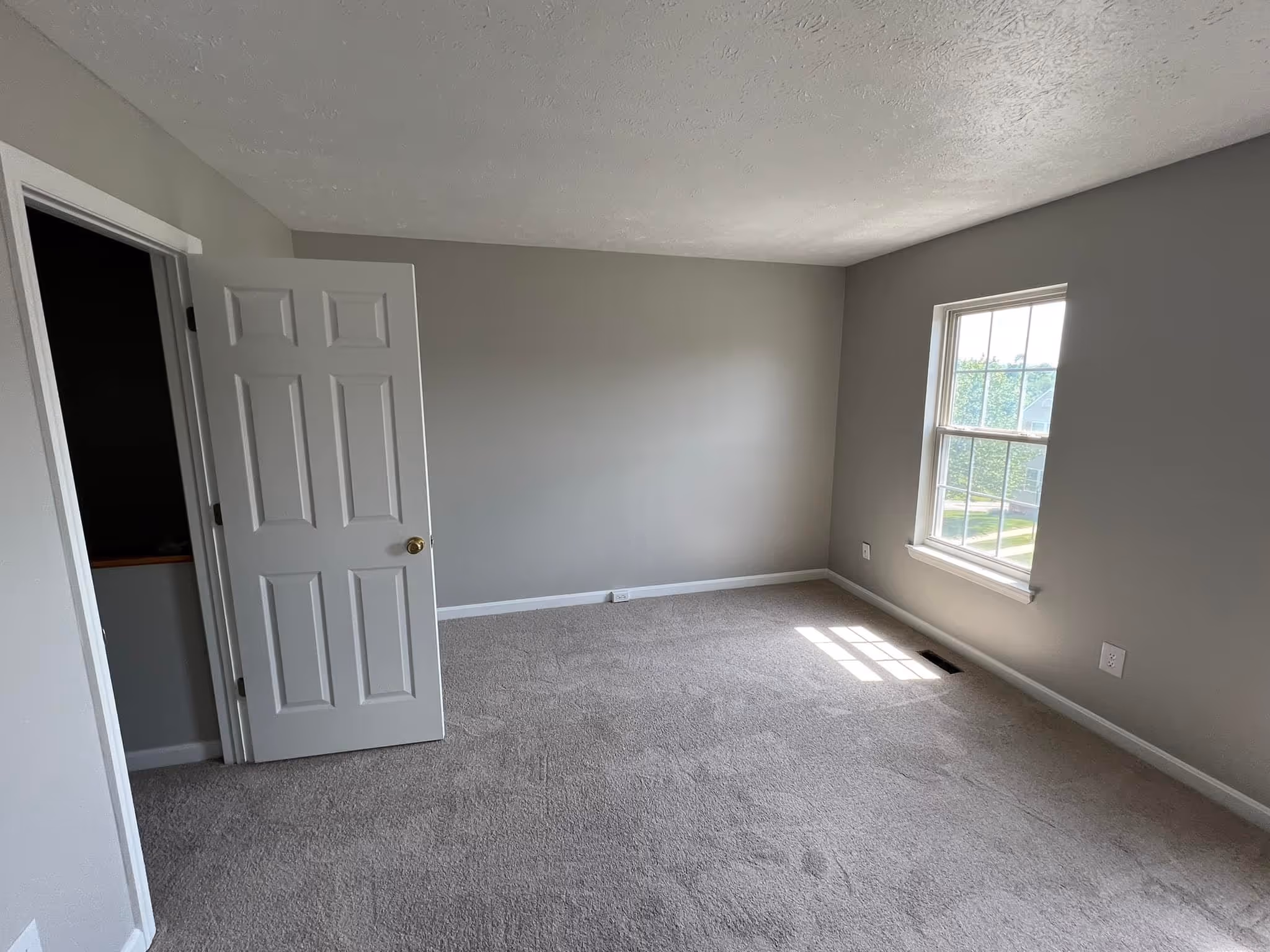 Interior view of a room with wooden floor, white staircase with dark brown railing, and an adjacent kitchen.