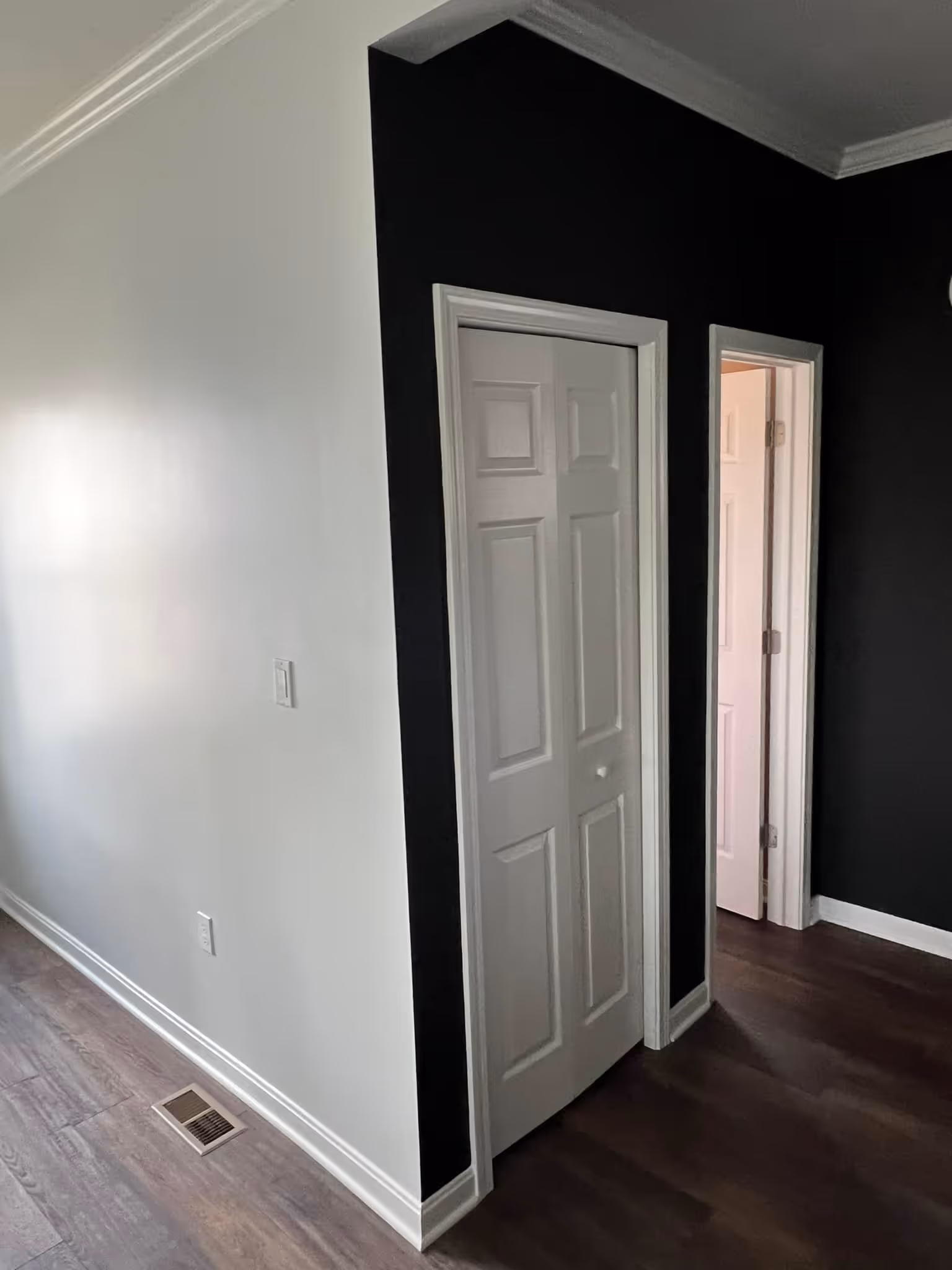 Interior corner of a room with white and black walls, white doors, and dark wood flooring.