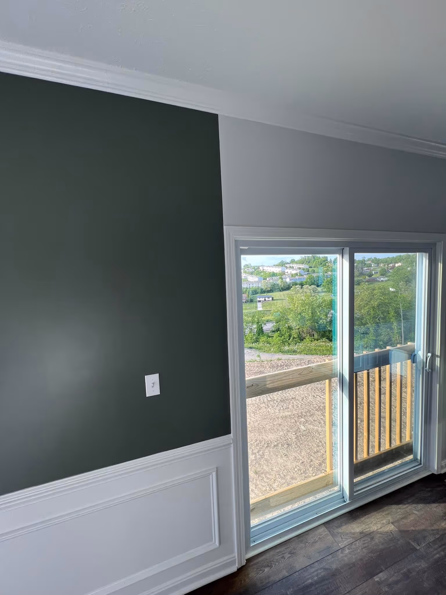 Interior corner of room with dark green and white walls next to a sliding glass door leading to a balcony.