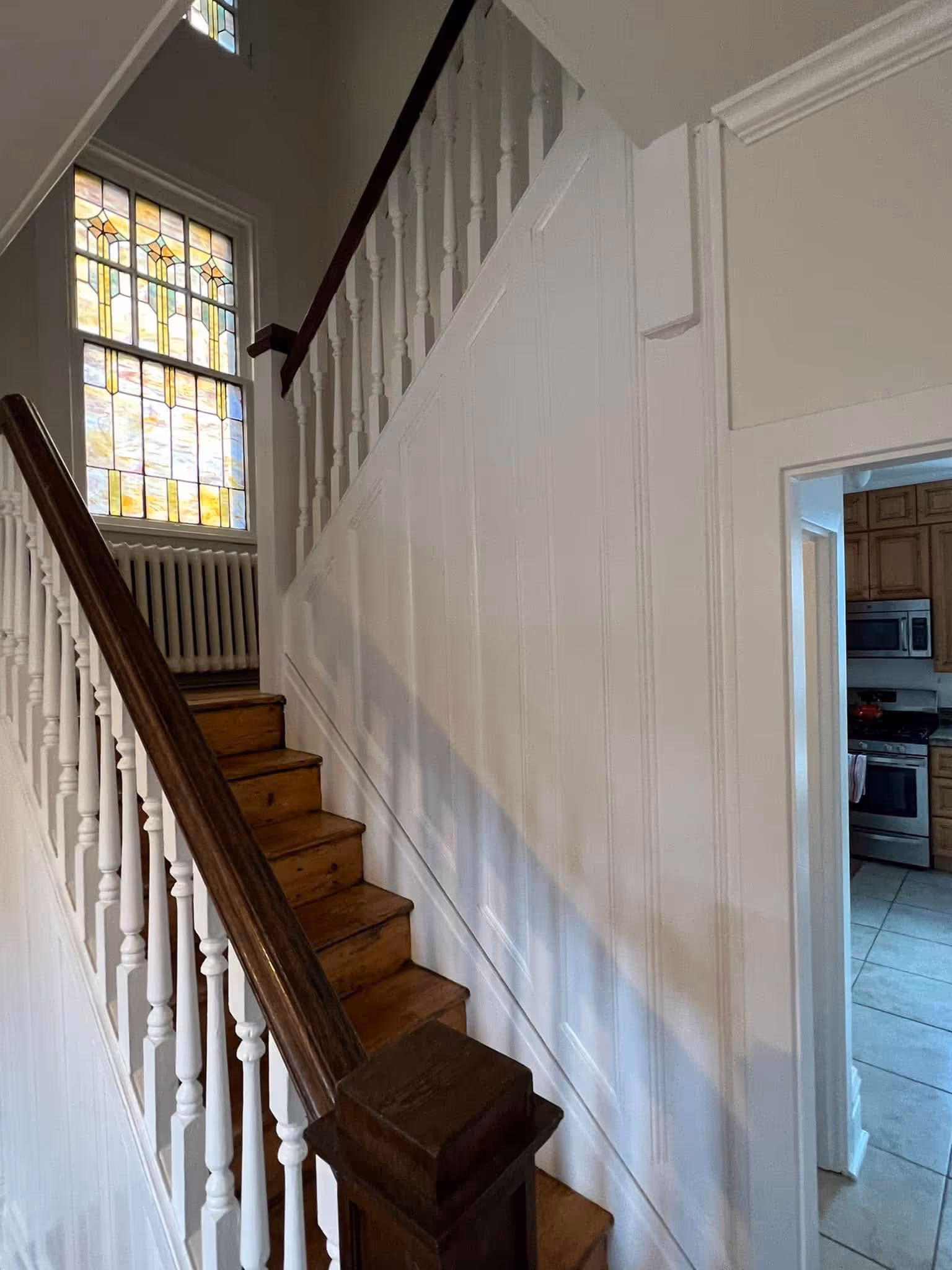 Wooden staircase with white balusters and a stained glass window at the top in a house interior